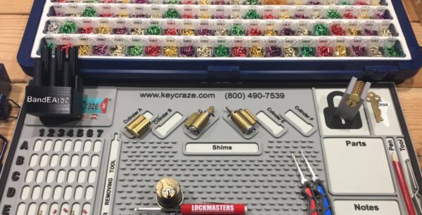 Image of a lock rekeying pinning mat, a case of colorful cylinder pins, assorted tools, and key cylinders.